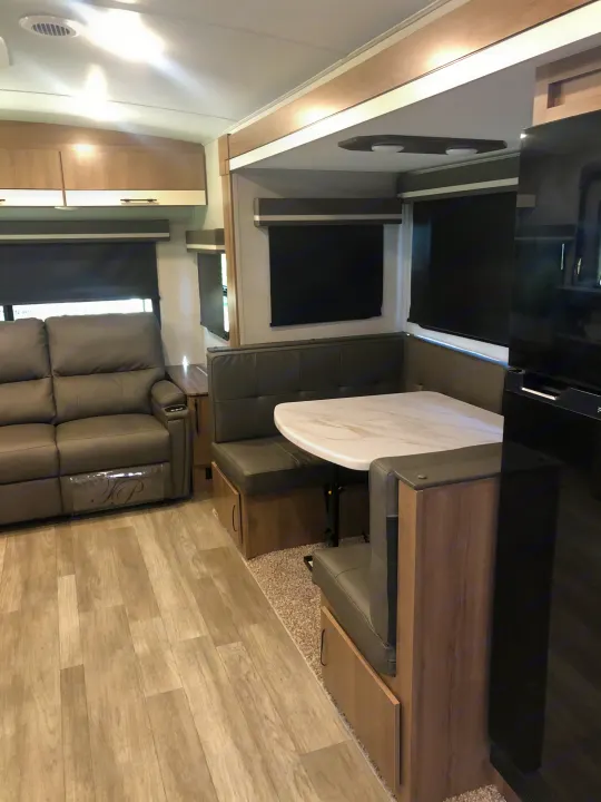 Comfortable modern rv rental interior with wood floors, a sofa, and a dinette.. Grand Design Imagine 2023
