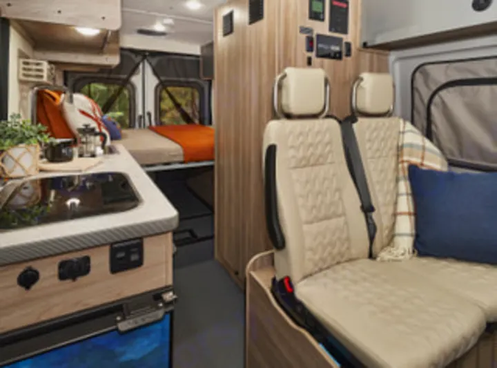 This modern RV rental features a campervan interior, showing swiveling front seats, a compact kitchen, and a rear bedroom.. Winnebago Solis PX 2025