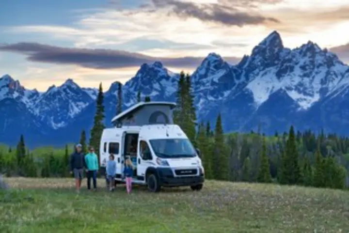 A family of four and their white RV rental camper van with pop-top are set against majestic snow-capped mountains.. Winnebago Solis PX 2025