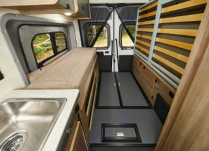 RV rental van interior: A compact living space with a bed on the left, kitchenette, and wood-paneled storage on the right.. Winnebago Solis PX 2025