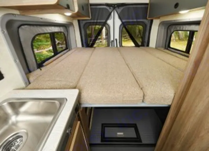 Cozy RV rental camper van interior featuring an elevated bed over storage, a sink, and scenic window views. Great for travel!. Winnebago Solis PX 2025