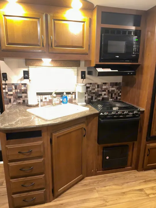 Cozy RV rental kitchen with light wood cabinets, microwave, stovetop, sink, and mosaic backsplash. Perfect for travel.. Jayco Jay Flight 2016
