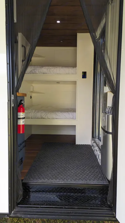 View into a cozy RV rental interior with practical bunk beds, a mounted fire extinguisher, and compact living amenities.. Diamond Cargo 16x8.5 2023