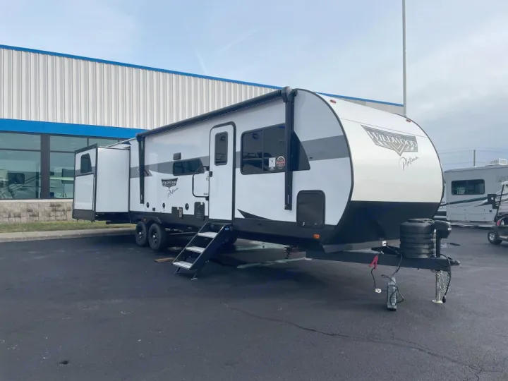 White Wildwood travel trailer with slide-outs extended, parked at a dealership. Explore this RV rental.. Forest River Wildwood 2024