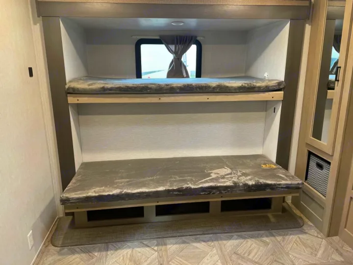 RV rental bunk beds: a neat two-tier sleeping area with mattresses, a window, and shelving for comfort.. Forest River Wildwood 2024