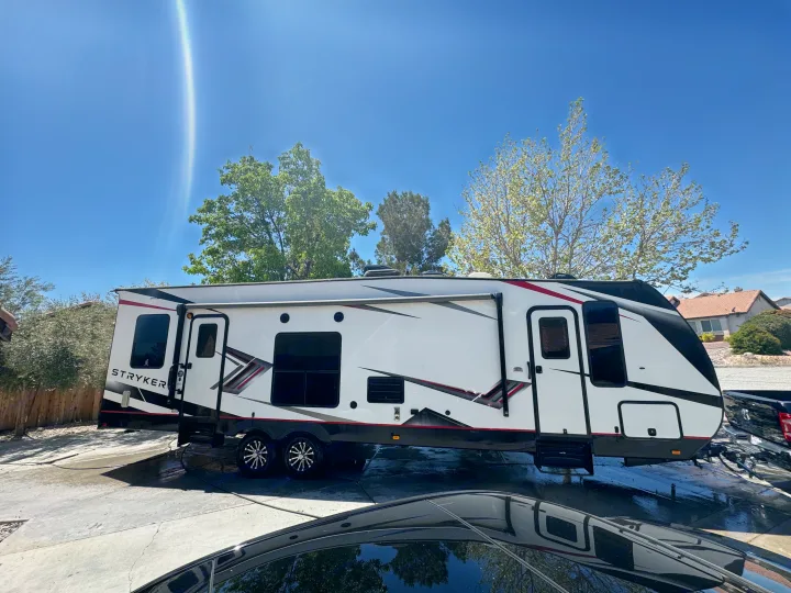 This large white Stryker RV, a potential rv rental, gleams in the sun on a wet driveway, fresh from a wash. Blue sky and trees surround it.. Cruiser Rv Corp Stryker 2021