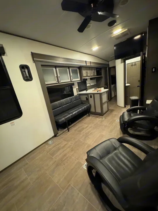 Spacious RV rental interior with modern living and kitchen areas, featuring a sofa, two recliners, and tiled floor.. Cruiser Rv Corp Stryker 2021