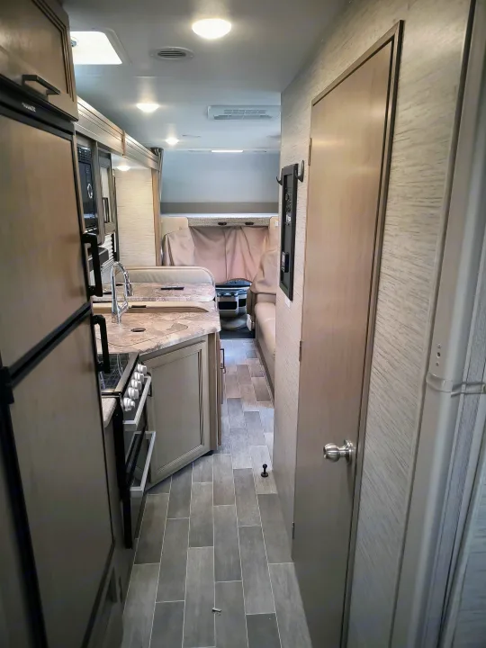 Bright interior of an RV rental, featuring a full kitchen with fridge & stove, dining area, and overhead bed in a modern design.. Thor Motor Coach Mgnitude 2022