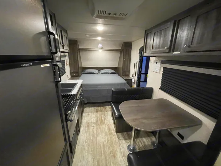 This RV rental interior shows a kitchen on the left, a bed in the back, and a dinette with seating on the right.. Highland Ridge RV Open Range 2019