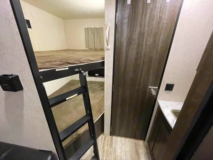 RV rental bunk beds with ladder, beside a wooden door and compact bathroom sink.. Highland Ridge RV Open Range 2019