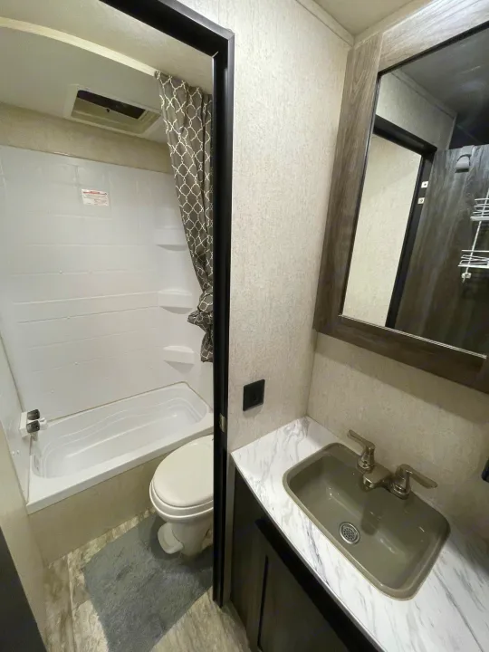Inside an RV rental bathroom: a well-maintained space with a tub/shower, toilet, and vanity with sink & mirror.. Highland Ridge RV Open Range 2019