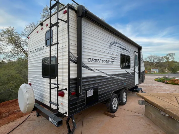 A modern Open Range travel trailer RV in white and black, featuring a rear ladder and side awning, perfect for rv rental trips.. Highland Ridge RV Open Range 2019