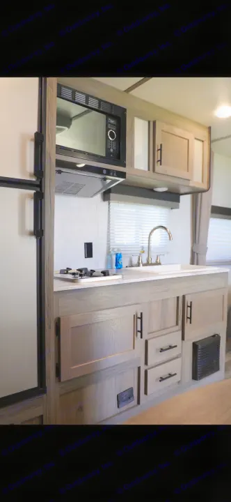 Explore this compact, modern RV rental kitchen featuring a microwave, stovetop, sink, and sleek cabinets for your travels.. Gulf Stream Enlighten 2022