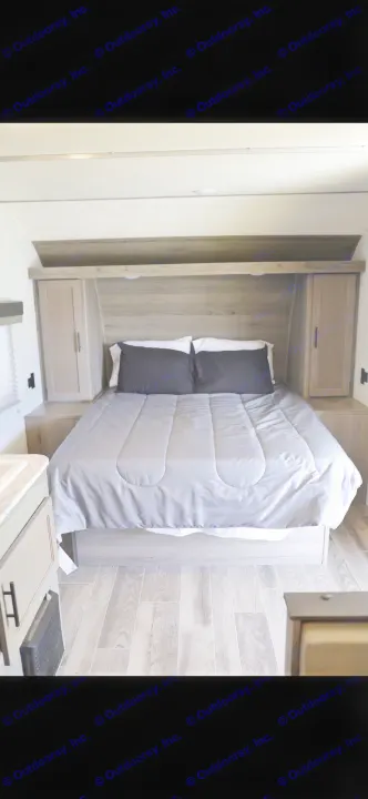 RV rental queen bedroom with modern wood-grain headboard, integrated storage, and light grey bedding.. Gulf Stream Enlighten 2022