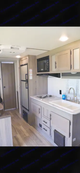 Bright RV rental interior. Modern kitchen with sink, stove, microwave, fridge, and light wood floors. Ready for travel.. Gulf Stream Enlighten 2022