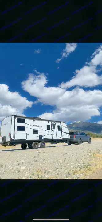 RV rental adventure: White Bullet travel trailer towed by an SUV, parked on a dirt road with mountains and blue sky.. Keystone RV Bullet Crossfire 2021