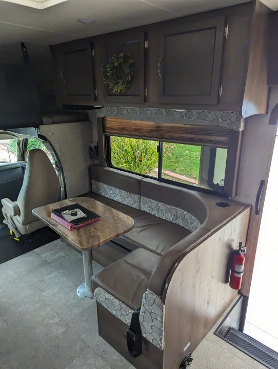 RV rental interior: dinette booth with table, overhead cabinets, and view into the front cab area.. Forest River Coachmen Freelander 2020