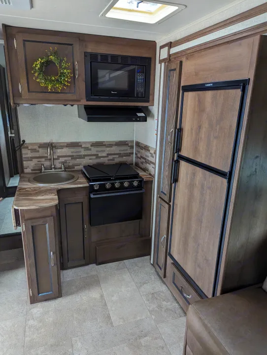 Compact RV rental kitchen: wood-look cabinetry, sink, stove, microwave, Dometic refrigerator, and tiled backsplash.. Forest River Coachmen Freelander 2020