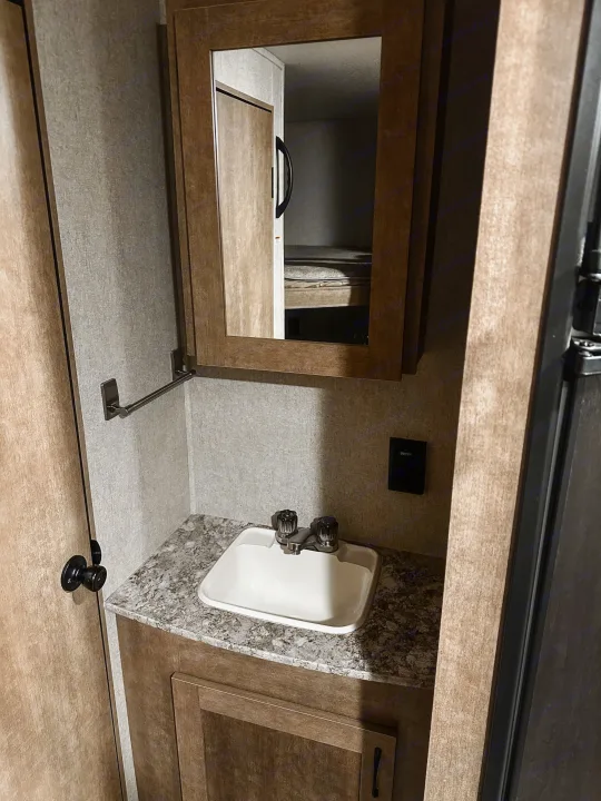 Compact RV rental bathroom features a sink, speckled countertop, mirrored medicine cabinet reflecting bunk beds, and wood cabinetry.. Starcraft AR-One Maxx 2017