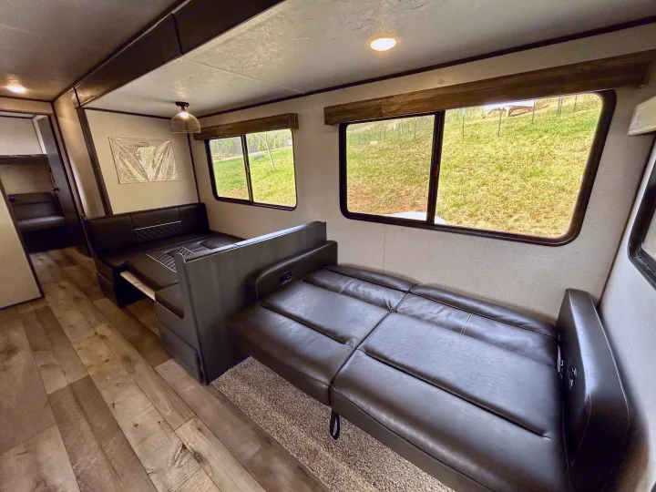 Interior view of an RV rental showing a comfy dinette with a table and an adaptable sofa bed. Features wood-look flooring.. Aspen Trail 3280BHS 2022