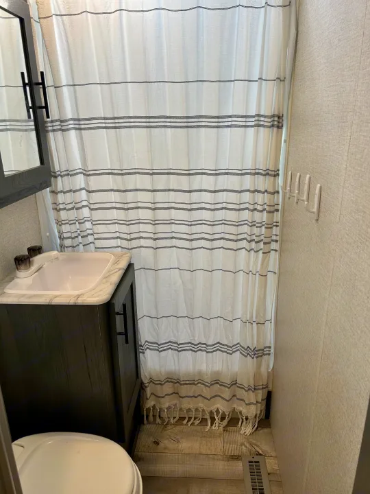 Modern RV rental bathroom with white and black striped shower curtain, white sink, dark vanity, and wall hooks.. Aspen Trail 3280BHS 2022