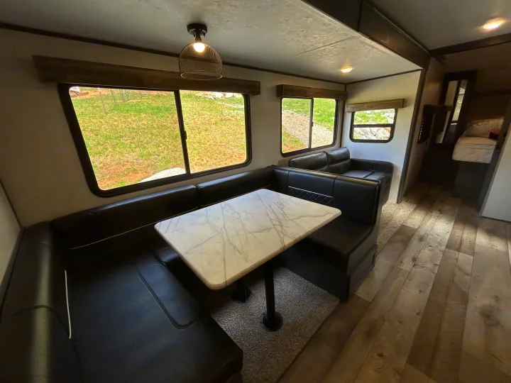 RV rental interior showcasing a black dinette with marble-patterned table, overlooking a grassy view, leading to the bedroom area.. Aspen Trail 3280BHS 2022