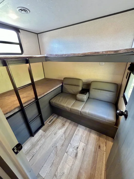 Comfortable bunk beds and sofa seating inside an RV rental. Features ladder, window, and wood-look floor.. Aspen Trail 3280BHS 2022