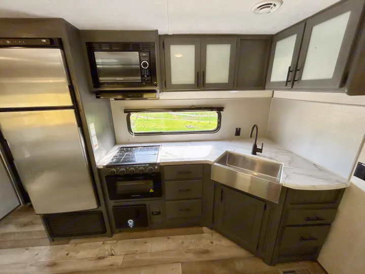 This modern RV rental kitchen boasts a large fridge, microwave, stove, and farmhouse sink with marble-look counters.. Aspen Trail 3280BHS 2022