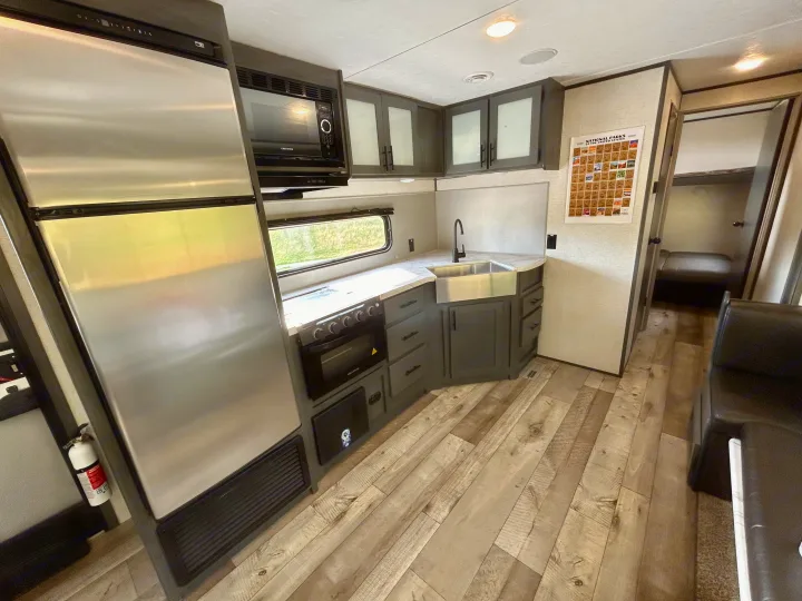 Explore the well-equipped kitchen in this RV rental, featuring a fridge, microwave, stove, sink, and cozy living space.. Aspen Trail 3280BHS 2022
