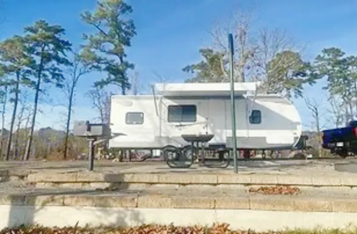 White RV rental travel trailer on a terraced campsite with an extended awning, grill, and picnic table. Ready for camping!. Shasta Oasis 2021