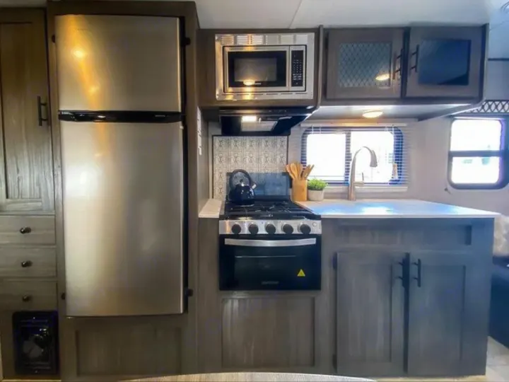 Modern RV rental kitchen showcasing a stainless steel fridge, oven, microwave, and sink with ample storage.. Shasta Oasis 2021