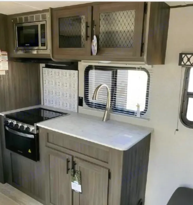 RV rental kitchen interior: Stainless steel microwave, stove, sink, and stylish cabinets with a patterned backsplash.. Shasta Oasis 2021