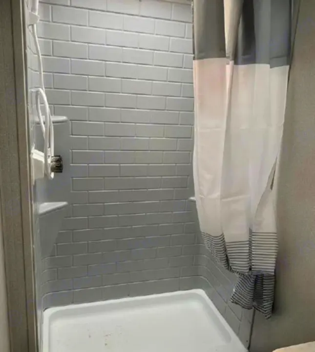 Inside your RV rental: a clean, functional shower with grey subway-style walls, white fixtures, and striped curtain.. Shasta Oasis 2021