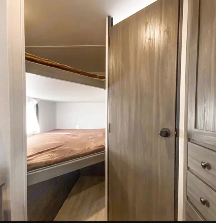 Inside an RV rental: Bunk beds are on the left, while a wooden door and drawers are seen on the right.. Shasta Oasis 2021