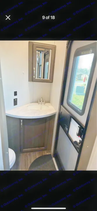 RV rental compact bathroom with corner sink, vanity, mirrored cabinet, toilet, and exterior door view.. Keystone RV Cougar 2021