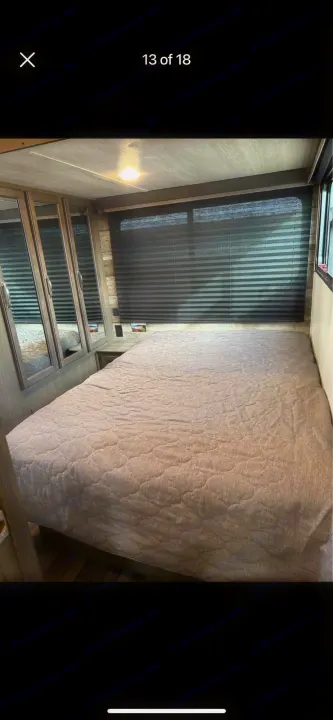 This RV rental offers a compact bedroom with a quilted bed, mirrored cabinets, and wide window blinds.. Keystone RV Cougar 2021