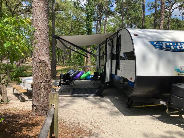 An RV rental at a serene, treed campsite with an extended awning, picnic table, and outdoor equipment.. Forest River Salem Cruise Lite 2023