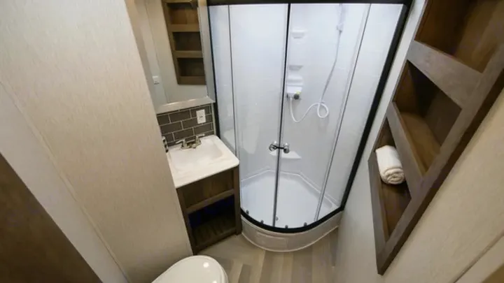Compact modern RV rental bathroom featuring a corner shower, vanity, sink, toilet, and stylish shelving.. Forest River Wildwood 2021