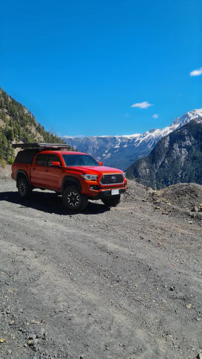 Vibrant orange pickup with rooftop tent on a scenic mountain road. Imagine this adventure as an RV rental, exploring wild landscapes.. Toyota Tacoma TRD OFF ROAD 2018