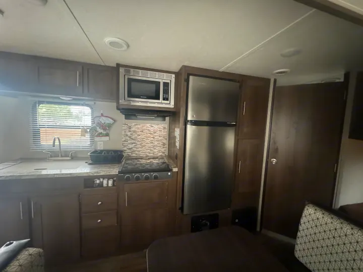 Modern rv rental kitchen with stainless steel microwave, large refrigerator, sink, and stovetop, fully equipped for travel.. Shasta 26db 2020