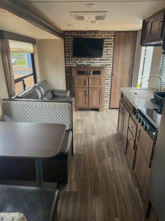 Spacious RV rental interior featuring a cozy dining booth, comfortable sofa, entertainment center with TV, and a functional kitchen.. Shasta 26db 2020