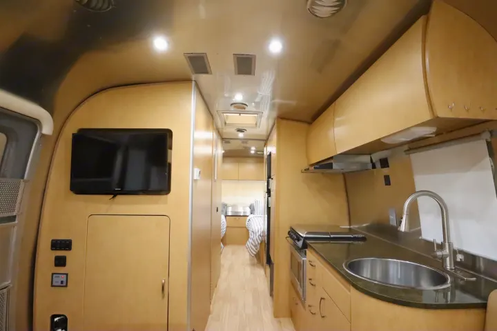 Inside an RV rental, showing the compact kitchen with sink and stovetop, a TV in the living area, and the bedroom beyond.. Airstream Flying Cloud 2016