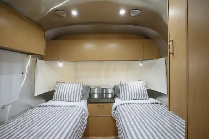Spacious RV rental bedroom with two cozy twin beds, striped duvets, and ample overhead storage. Bright and functional.. Airstream Flying Cloud 2016