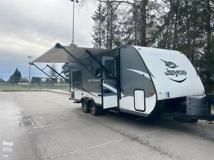 This white & grey Jayco Jay Feather RV rental, with its awning open, is parked in a lot, ideal for camping trips.. Jayco X213 2016