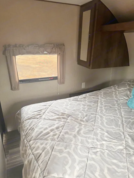 Cozy RV rental bedroom with a patterned comforter, window, and overhead storage, perfect for a comfortable travel stay.. Shasta 26db 2020