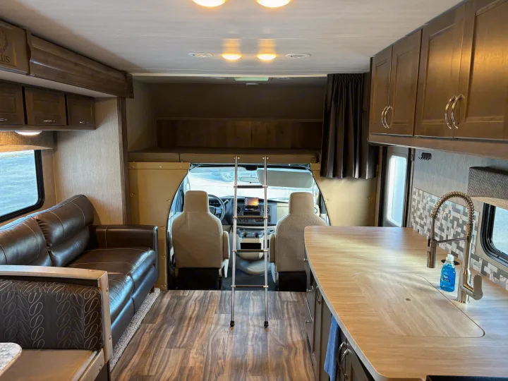 Interior of an rv rental, highlighting the functional kitchen, inviting sofa, and convenient over-cab bunk.. Nexus RV Triumph 2021
