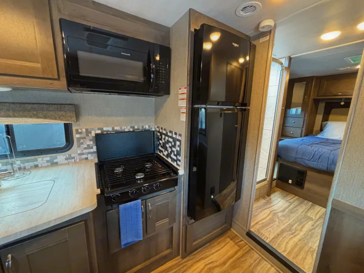 Compact RV rental interior: a kitchen with microwave, stove, and refrigerator, leading to a cozy bedroom area.. Nexus RV Triumph 2021