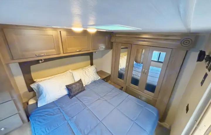 Inside a comfortable RV rental bedroom, featuring a bed, overhead cabinets, and mirrored closet. Ideal for travel.. Nexus RV Triumph 2021