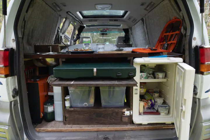 RV rental: Camper van's rear kitchen setup with sink, stove, open fridge, and pastries. Ready for camping meals on the road.. nissan elgrand 1997