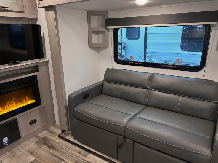 RV rental interior: A cozy gray sofa, electric fireplace with warm glow, and TV create a comfortable space.. 4YDTCMH25RJ935536 1805RB 2024